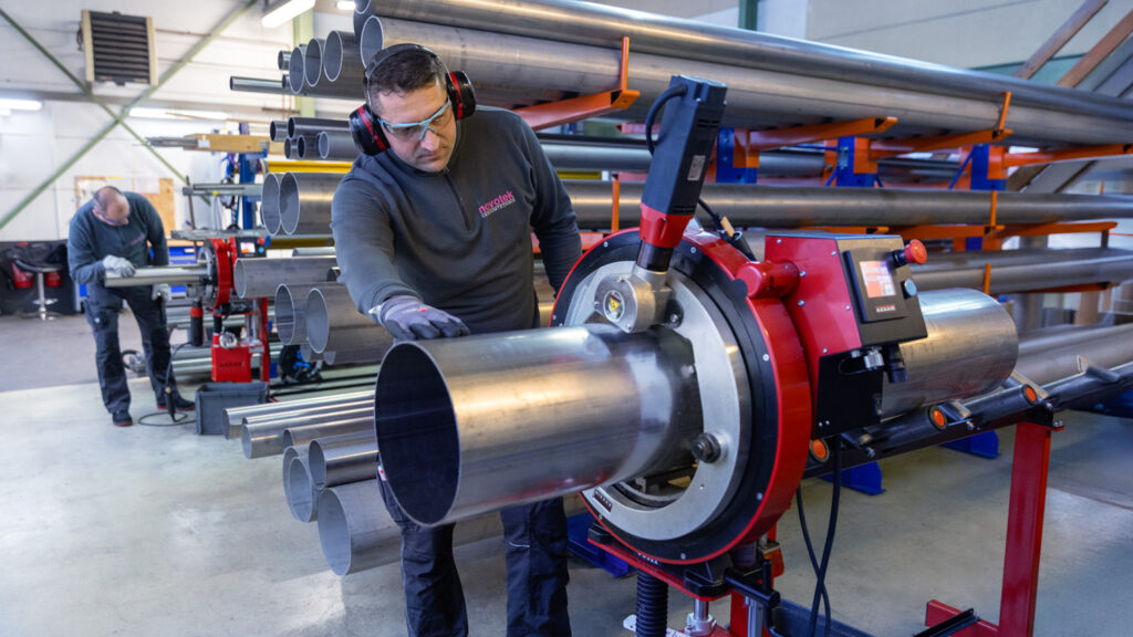 Mitarbeiter an Orbitalsäge. im Hintergrund großes Rohrlager